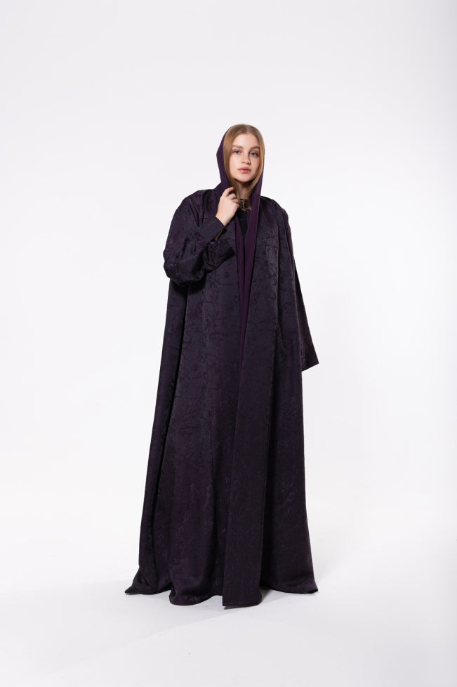 Deep purple abaya made from premium jacquard fabric with a subtle textured pattern, featuring a flowing cut and refined detailing.