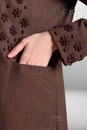 Deep brown coat-style abaya with front buttons, side pockets, and hand-embroidered detailing for a refined and stylish look.