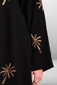 Black abaya with intricate gold embroidery featuring a palm tree motif in golden thread, exuding elegance and luxury.