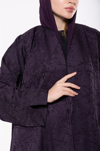 Deep purple abaya made from premium jacquard fabric with a subtle textured pattern, featuring a flowing cut and refined detailing.
