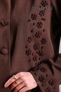 Deep brown coat-style abaya with front buttons, side pockets, and hand-embroidered detailing for a refined and stylish look.