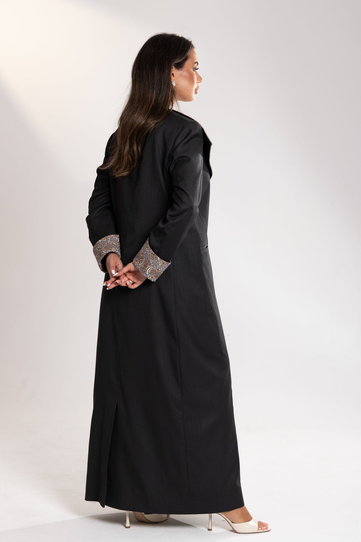 Woman wearing a long black coat with patterned cuffs on from esme abaya qatar