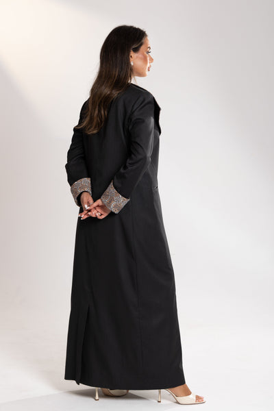 Woman wearing a long black coat with patterned cuffs on from esme abaya qatar