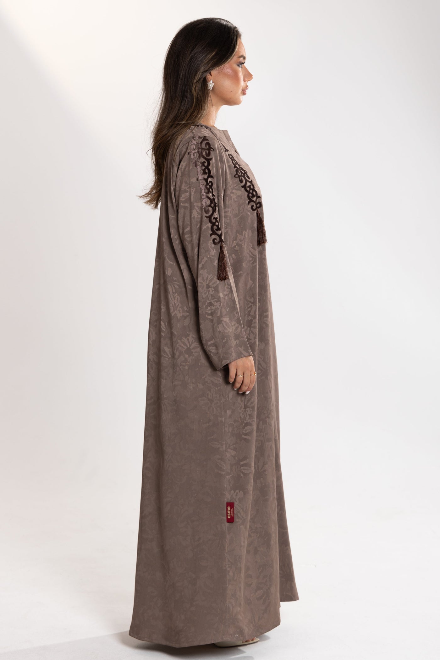 Woman wearing a long brown esme abaya with intricate embroidery on a white background